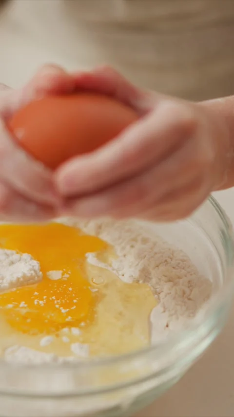 Close up of hands cracking egg into bowl with flour for baking showing Stock Footage 346795301