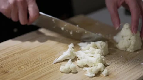 Close-up of hands cutting fresh cauliflower on wooden board with kitchen knife Stock Footage 315236825