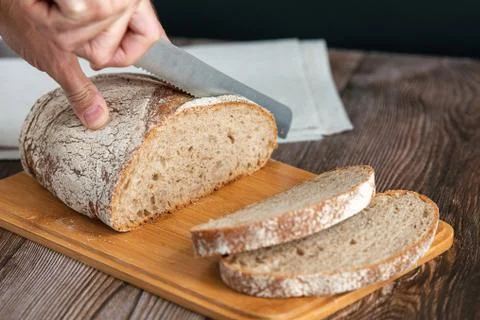 Close up of hands cutting a slice of bread. Male hands cutting bread on wooden Stock Photos