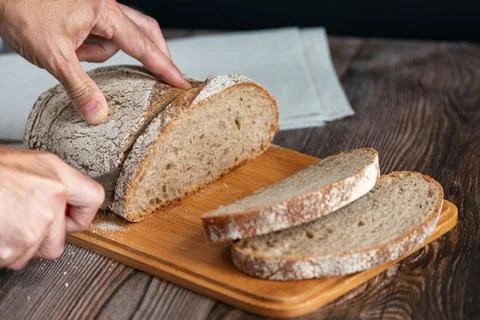 Close up of hands cutting a slice of rey bread. Male hands cutting bread Stock Photos