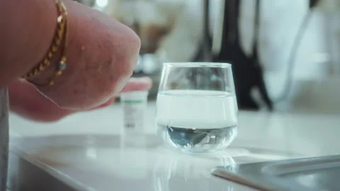 Close-up of hands dropping an effervescent tablet into a glass of water on .. Stock Footage 327624033