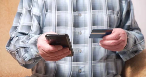 Close up of hands of an elderly man holding smartphone and credit card and doing Stock Footage 151012035