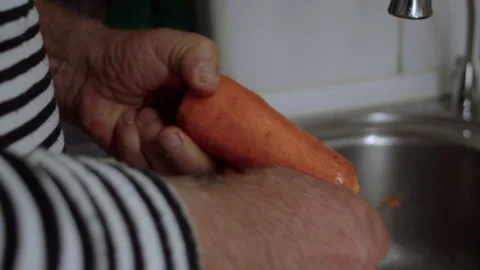 Close-up, hands of an elderly man peeling raw carrots with a knife over kitchen Stock Footage 318806260