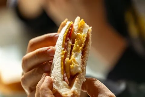 Close-up of hands enjoying a sandwich, a backlit breakfast scene, a documen.. Fotos Stock