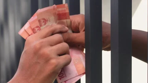 Close-up of hands exchanging Indonesian rupiah through prison bars Stockbeeldmateriaal 335335865