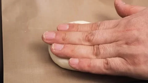 Close-Up of Hands Flattening a Round Dough Ball on a Brown Baking Mat Stock Footage 331632603