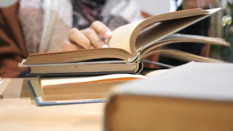 Close up of hands flipping through aged books on wooden table, soft focus b.. 스톡 동영상 332578769
