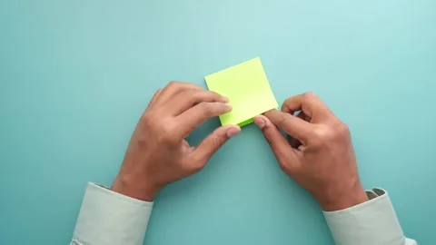 Close-up hands folding fluorescent sticky note on turquoise background, sta.. Stock Footage 332407453