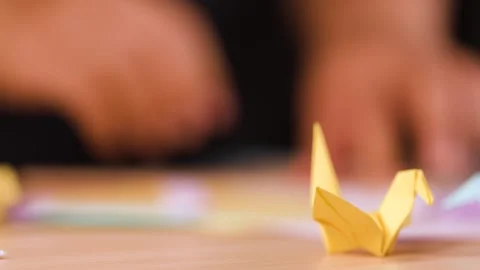 Close Up of Hands Folding Origami Paper Crane on Wooden Table Stock Footage 327258602