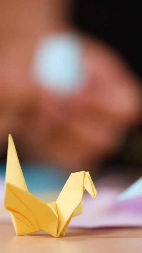 Close Up of Hands Folding Origami Paper Crane on Wooden Table Stock Footage 327258681