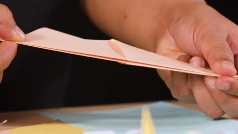 Close Up of Hands Folding an Origami Paper Airplane at a Table Stock Footage 327446535