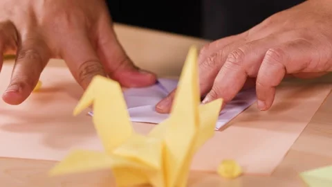 Close Up of Hands Folding a Paper Origami Crane on Table Stock Footage 327177221