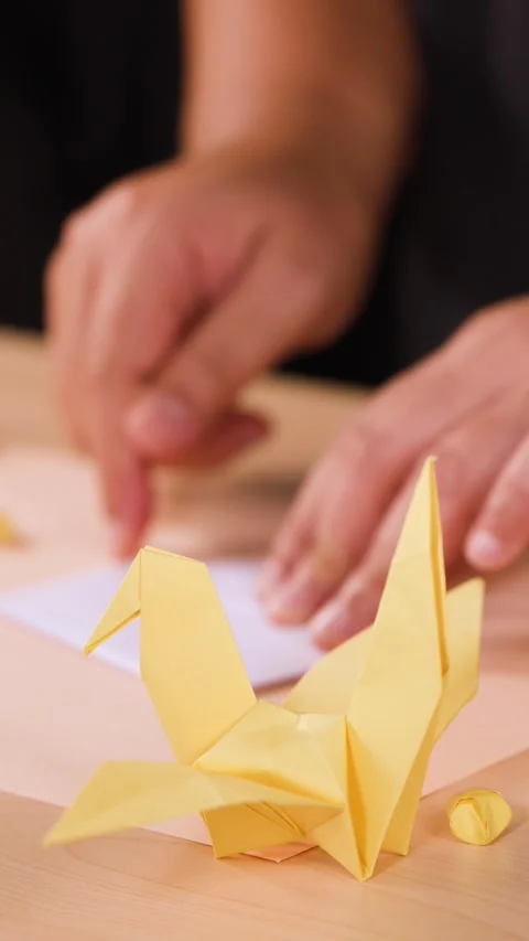 Close Up of Hands Folding Paper Origami Bird on Wooden Table Stock Footage 327186718