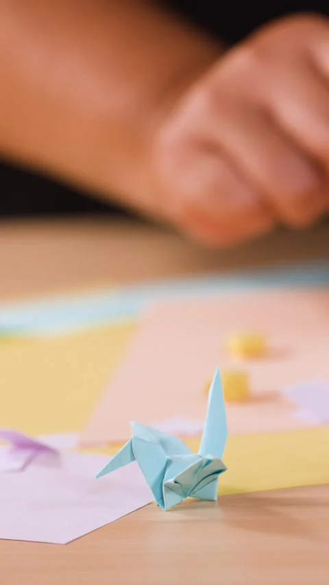 Close Up of Hands Folding Paper Origami Crane on Wooden Table Stock Footage 327260845