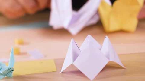 Close Up of Hands Folding Paper Origami Figures on a Wooden Table Stock Footage 327626518