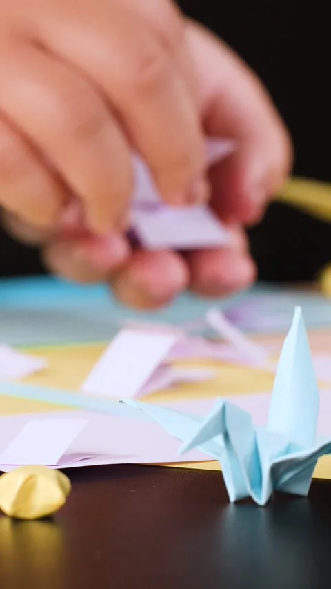Close Up of Hands Folding Small Paper Origami Cranes on Table Stock Footage 327710630
