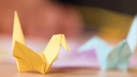 Close Up of Hands Folding Yellow Paper Origami Bird on Table Stock Footage 327121119