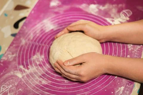 A close-up of hands gently cupping and shaping a smooth ball of dough on a .. Stock Photos