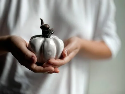Close up of hands gently holding small white ceramic pumpkin with twisted brown Stock-Fotos