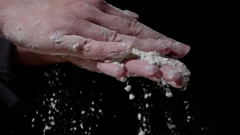 Close-up of hands gently sprinkling flour, creating a cloud of dust against a Video stock 301647549