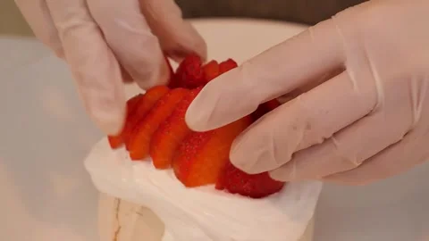 Close-up of hands in gloves decorating a mini pavlova with fresh sliced strawber Stock Footage 331782204