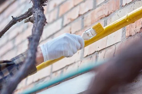 Close up of hands in gloves paint a yellow tube outside. Spring rustic works Stock Photos