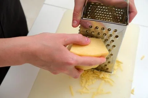 Close-up of hands grating a block of hard cheese using a stainless steel bo.. Stock Photos