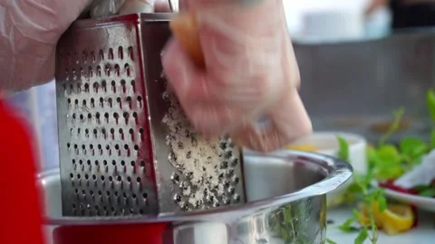 Close-up of hands grating fresh ingredients using a metal grater, showcasing the Видео 330593603