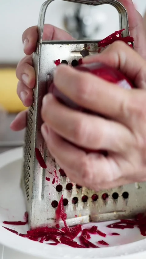 A close-up of hands grating a red beet on a metal grater, showcasing vibrant Stock Footage 317711981