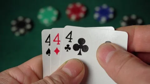 Close-up of hands gripping playing cards displaying three of a kind or set, with Stock Footage 332830399