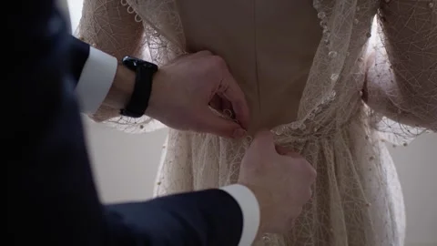 Close-up of the hands of groom fastens the buttons on the elegant bride's dress. Stock Footage 256656352