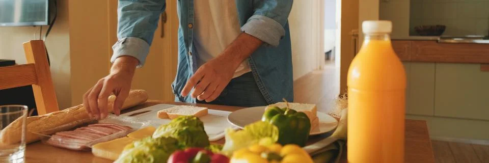 Close-up of the hands of guy dressed in denim shirt cooking sandwich while .. Stock Photos