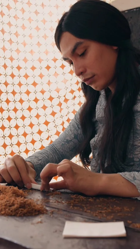 Close-up of Hands Hand-Rolling a Cigarette with Batik Background Video stock 262519342