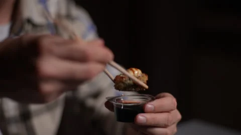 Close-up hands of handsome man dipping sushi rolls in soy sauce bowl with Stock Footage 263477624