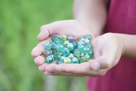 Close up hands hold round small marble balls, spherical objects often made from  Stock Photos