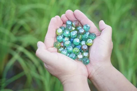 Close up hands hold round small marble balls, spherical objects often made from  Stock Photos