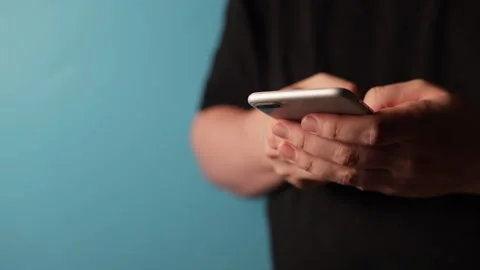 Close-up of hands holding and interacting with a smartphone against a blue Stock Footage 340265641