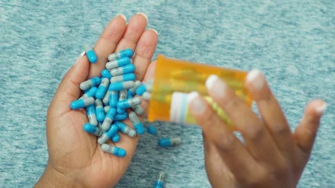 Close-up of hands holding and pouring blue and white pills from a container Stock Footage 314964347
