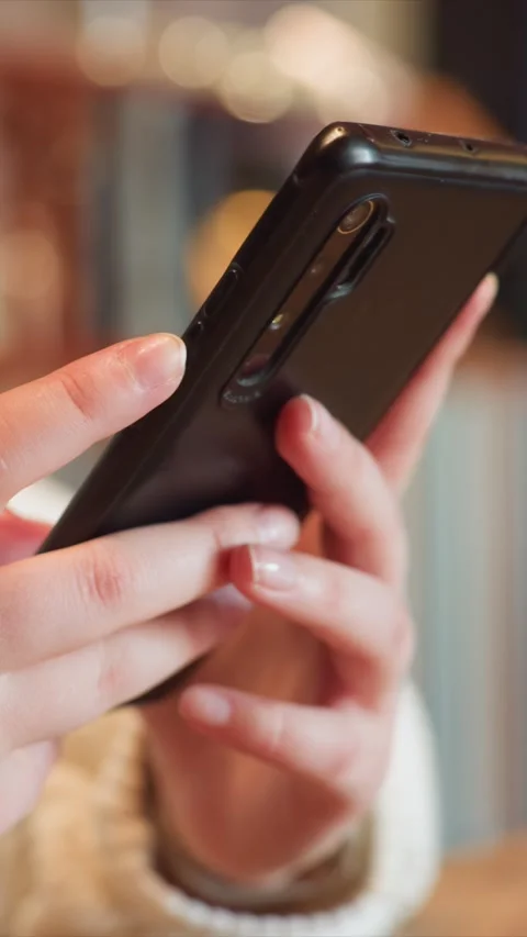 Close up of hands holding and using smartphone in warm cafe lighting featuring Stock Footage 348175554
