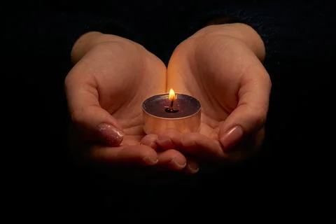 Close-up of hands holding a burning candle in the dark. Adult woman with a .. Stock Photos