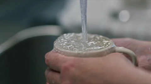 Close-up of hands holding a ceramic mug under running tap water in a kitche.. Stock Footage 344578855