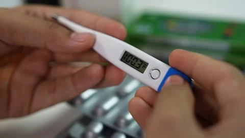 Close-up of hands holding a digital thermometer showing fever reading, with.. Stock Footage 330547509