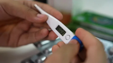 Close-up of hands holding a digital thermometer showing a fever reading, me.. Stock Footage 330547515