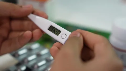 Close-up of hands holding a digital thermometer showing fever temperature, .. 库存影片 330547518