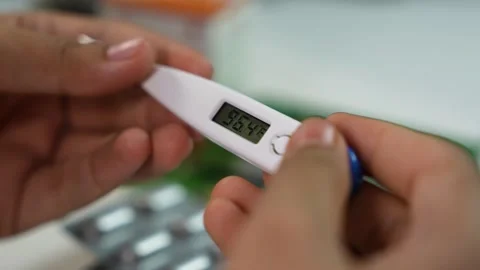 Close-up of hands holding a digital thermometer with fever reading, blurred.. Stock Footage 330547520