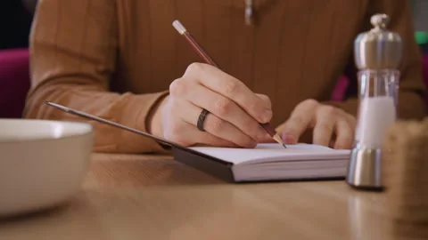 Close up of hands holding freshly sharpened red pencil over open notebook on Stock Footage 344871008