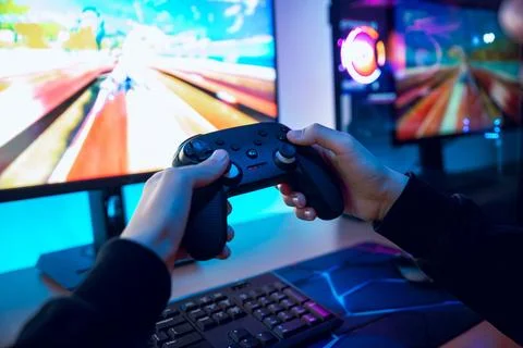Close up of hands holding game controller while racing video game runs on c.. Stock Photos