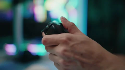 Close-up of hands holding gamepad controller, playing videogame on computer in Stock Footage 317828674