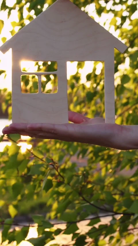 Close up of hands holding model of house through window of which setting sun Stock Footage 265605360