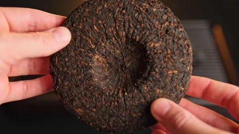 Close-up of hands holding a round compressed Pu-erh tea cake, showcasing its Stock Footage 295780288